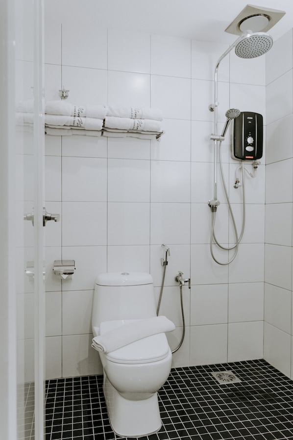 A modern bathroom with a white toilet, a shower with a handheld showerhead, and a black and white tiled floor. - MUO Resort (Muar)