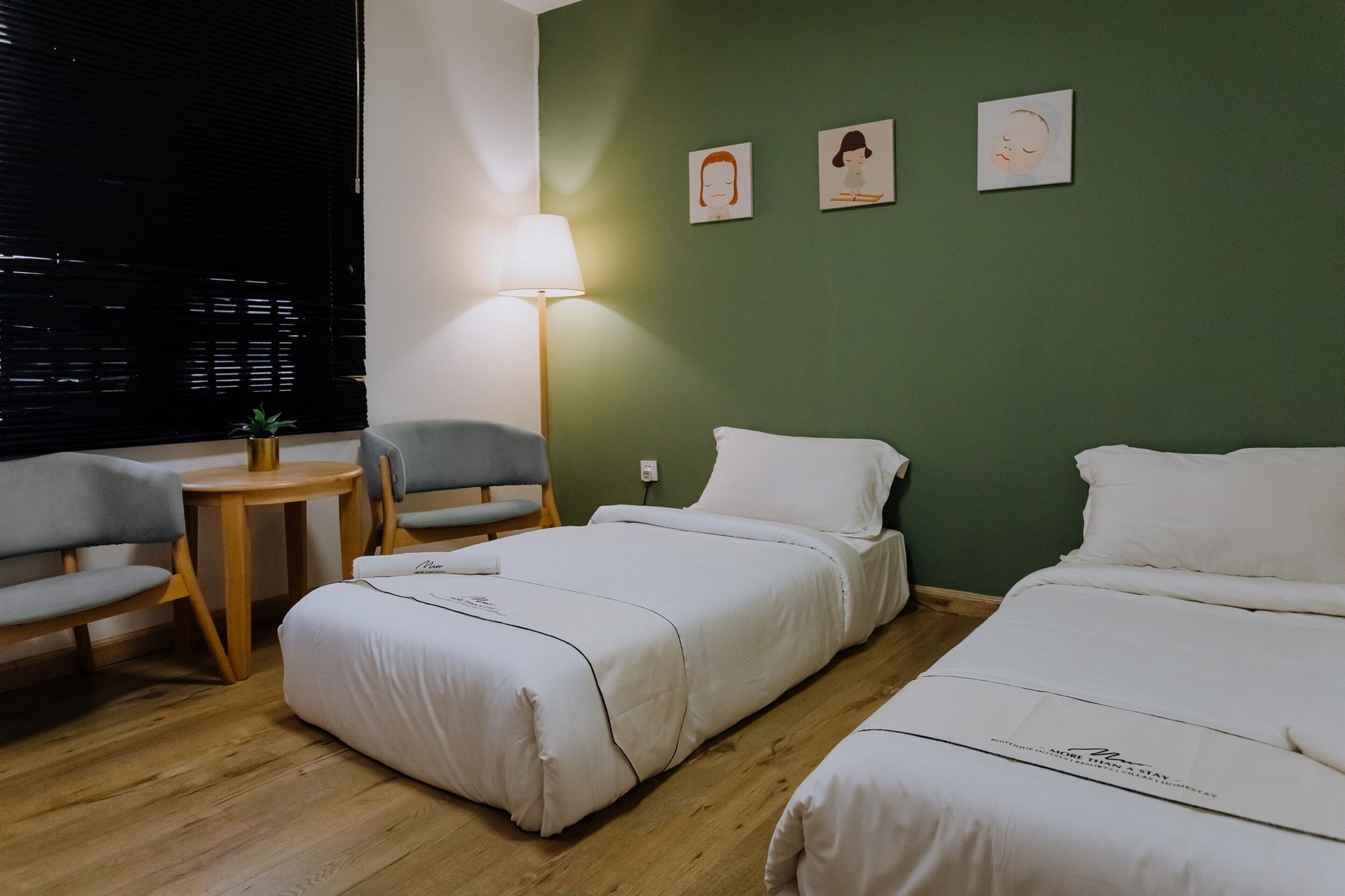 Habitación de hotel con dos camas, una mesita, dos sillas y una lámpara.