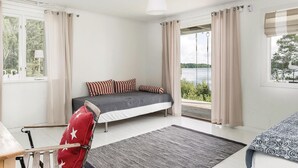 Une chambre avec un lit, une chaise, une fenêtre avec des rideaux, une vue sur un lac et un fauteuil suspendu à l’extérieur.