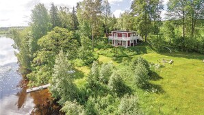 Une maison dotée d’un porche, entourée d’un paysage verdoyant luxuriant et bordée par un plan d’eau.