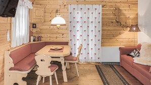 A cozy cabin interior with a wooden interior, a dining table with chairs, a sofa, and a lamp.