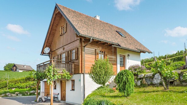 A two-story wooden house with a sloped roof, a balcony, and a stone wall.