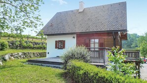 A small house with a sloped roof, a wooden porch, and a stone wall in the background.