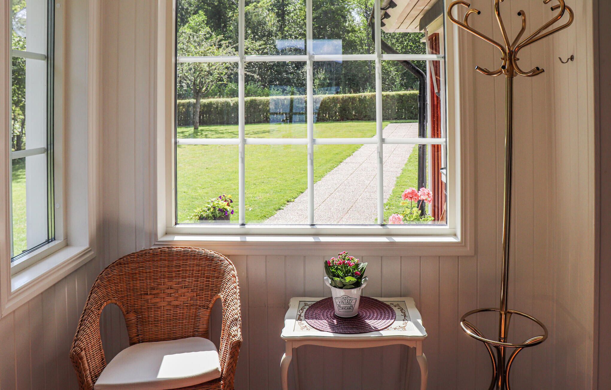 Ein Zimmer mit großem Fenster, Korbsessel, kleinem Tisch mit Topfpflanze und Stehlampe.