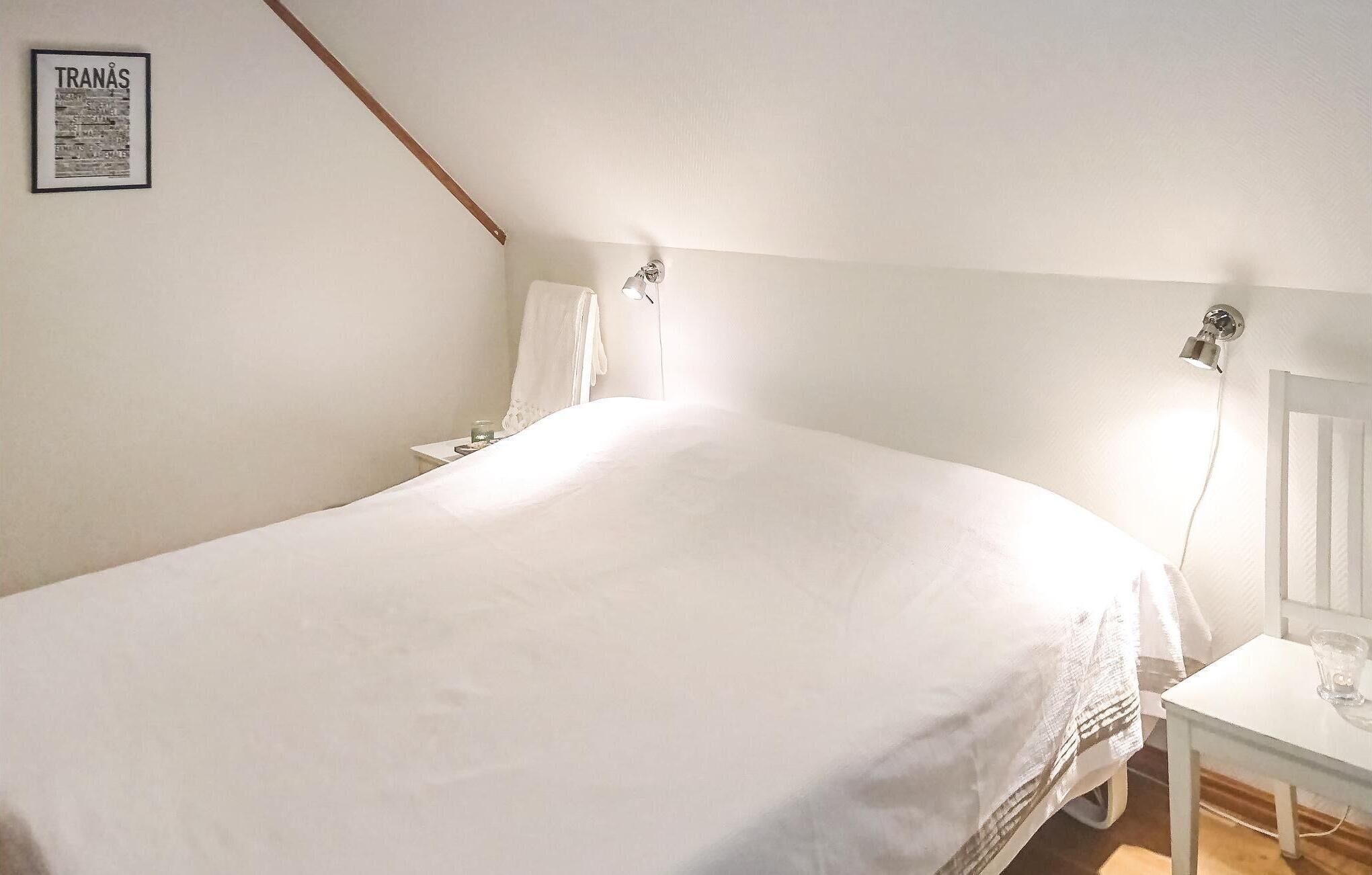 A bedroom with a large bed, a nightstand, a wall-mounted lamp, and a framed picture on the wall.