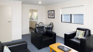 A modern living room with black leather sofas, a wooden coffee table, and a kitchen in the background. - Fitzgerald on King (Timaru)