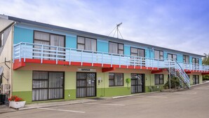 A motel with a blue and green facade, a red and white awning, and a staircase leading to a balcony. - Fitzgerald on King (Timaru)