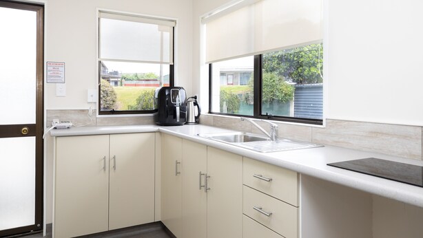 A kitchen with a sink, a coffee maker, and a window with a view of greenery. - Fitzgerald on King (Timaru)