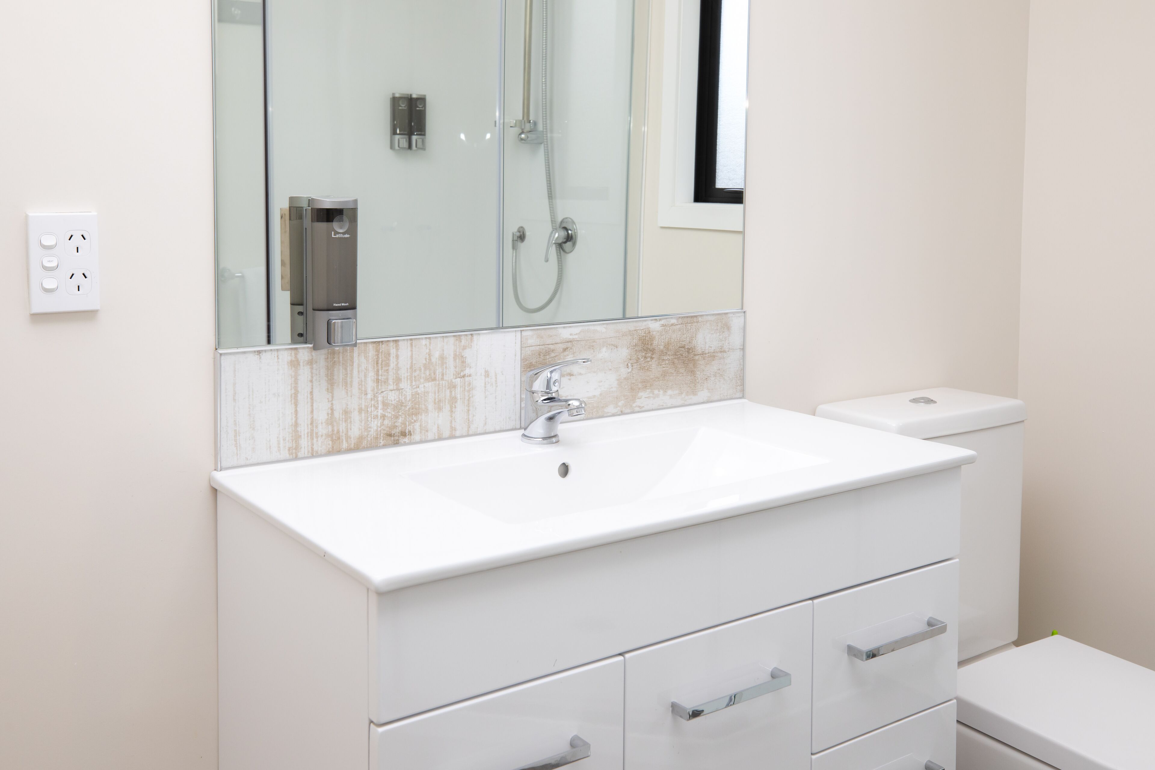 Un baño moderno con un lavamanos blanco, un espejo y una cabina de ducha de vidrio.