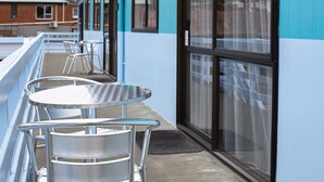A balcony with metal chairs and tables, a glass door, and a blue and white building facade. - Fitzgerald on King (Timaru)