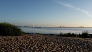 Ein Sandstrand mit ruhiger See und einem Schiff in der Ferne.