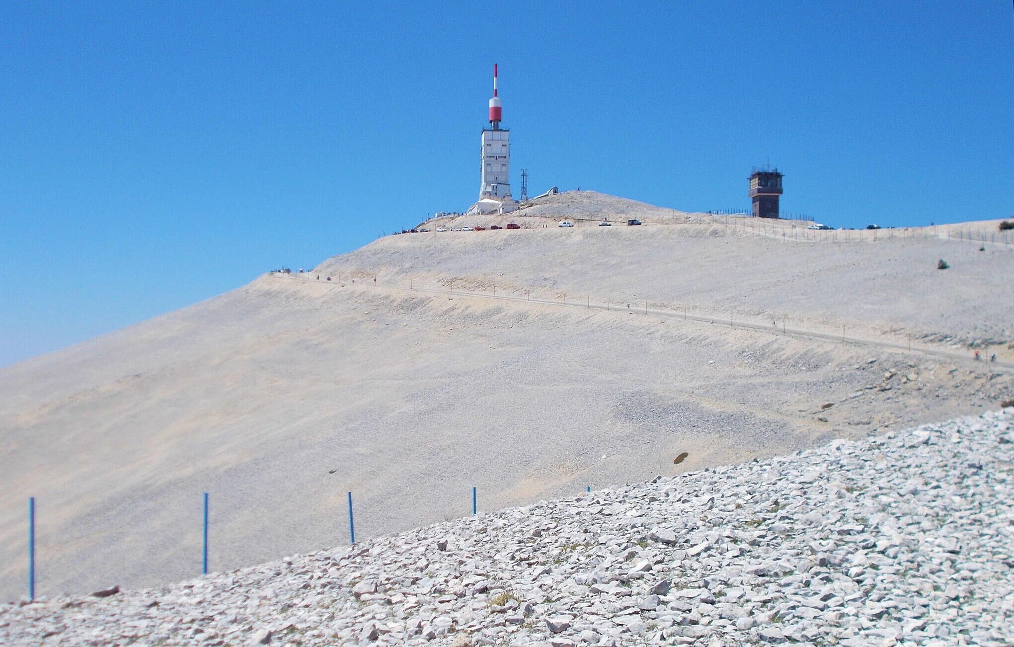 A barren hilltop with a tall structure featuring a red and white antenna, and a smaller building with a red roof.