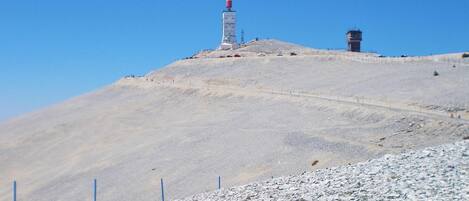 A barren hilltop with a tall structure featuring a red and white antenna, and a smaller building with a red roof.