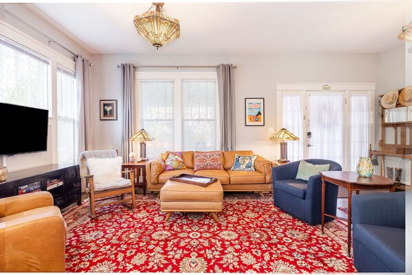 Una sala de estar con alfombra roja estampada, un sofá color beige, un sillón azul y una mesa de centro de madera.