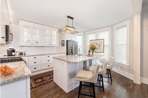 Una cocina moderna con armarios blancos, encimera de granito, una isla central con taburetes y una lámpara colgante.