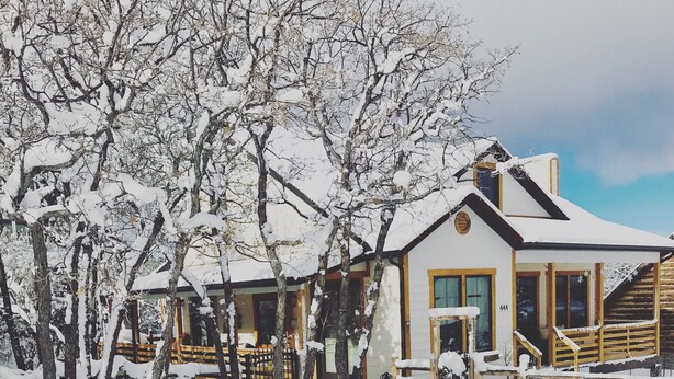A snow-covered lodge with a wooden exterior, a visible entrance, and a fenced yard. - Charming Mountain Cottage. (Pine Valley)