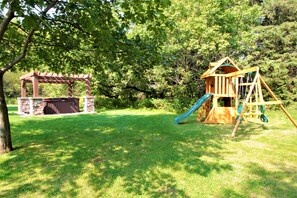 Guests can relax in a serene outdoor setting with a hot tub and enjoy playtime at a nearby wooden play structure.