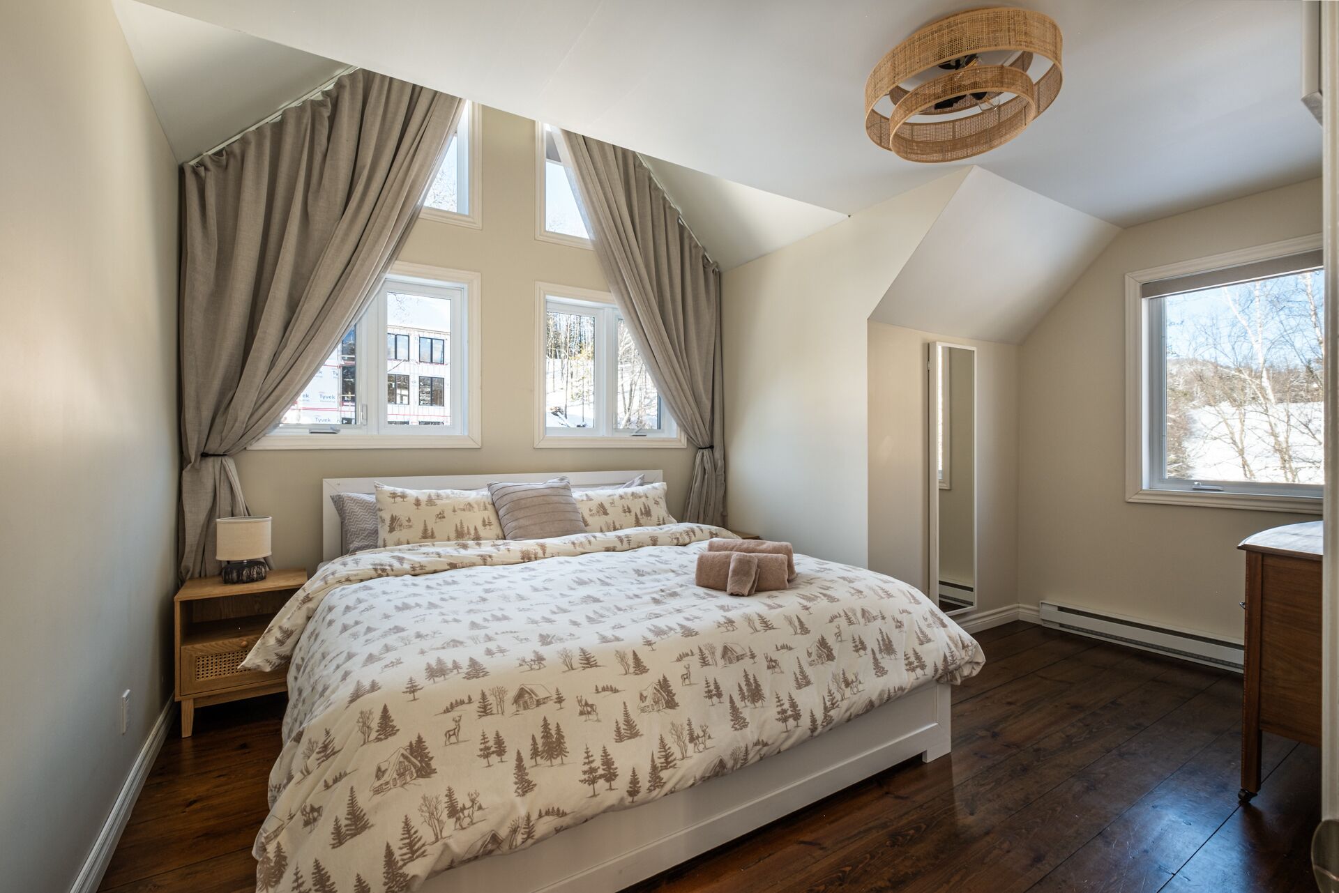 Un dormitorio con una cama grande, una mesita de noche, una lámpara y una ventana con cortinas.