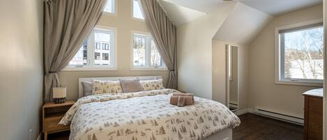 Un dormitorio con una cama grande, una mesita de noche, una lámpara y una ventana con cortinas.