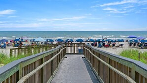 A wooden boardwalk leading to a beach with blue umbrellas and people relaxing. - Hot Tub, Pools, Wifi, Oceanfront, 7th Floor, AshWorth | AshWorth - 706 (North Myrtle Beach)