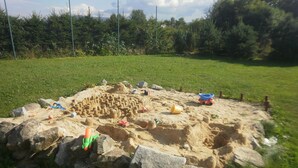 Un área de juegos con arena, un arenero, rocas y juguetes.