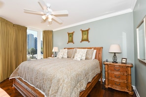 A bedroom with a large bed, a nightstand, a ceiling fan, and two framed pictures on the wall.