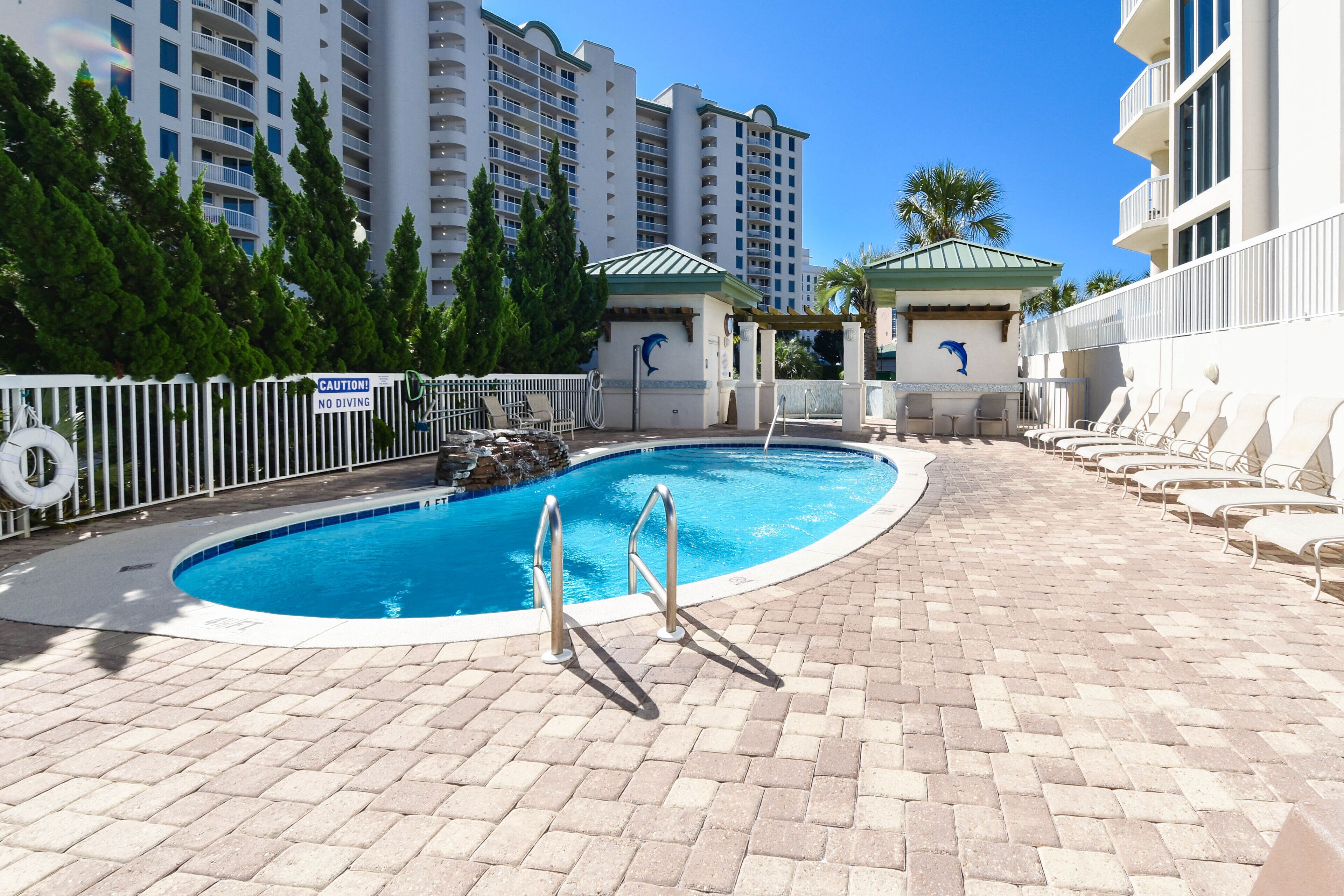 A pool area with a no diving sign, lounge chairs, and a building with a dolphin mural.