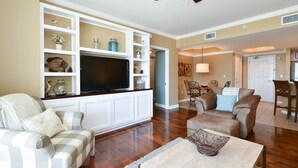A living room with a flat-screen TV, a sofa, a coffee table, and a dining area with chairs and a table. - Contemporary beachfront condo w/ poolside cabana in Destin! 🌴🐚 (Destin)