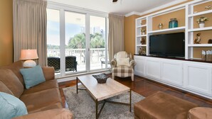 A living room with a sofa, armchair, coffee table, TV, and shelves with decorative items. - Contemporary beachfront condo w/ poolside cabana in Destin! 🌴🐚 (Destin)