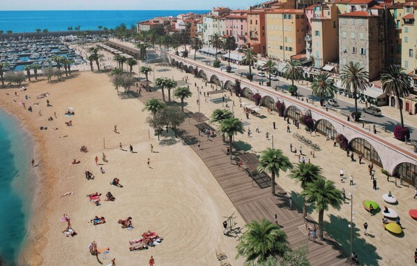 A beach with a promenade, palm trees, and buildings along the promenade.