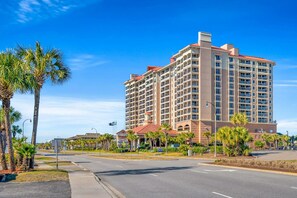A multi-story hotel with a central courtyard, surrounded by palm trees and a clear sky.