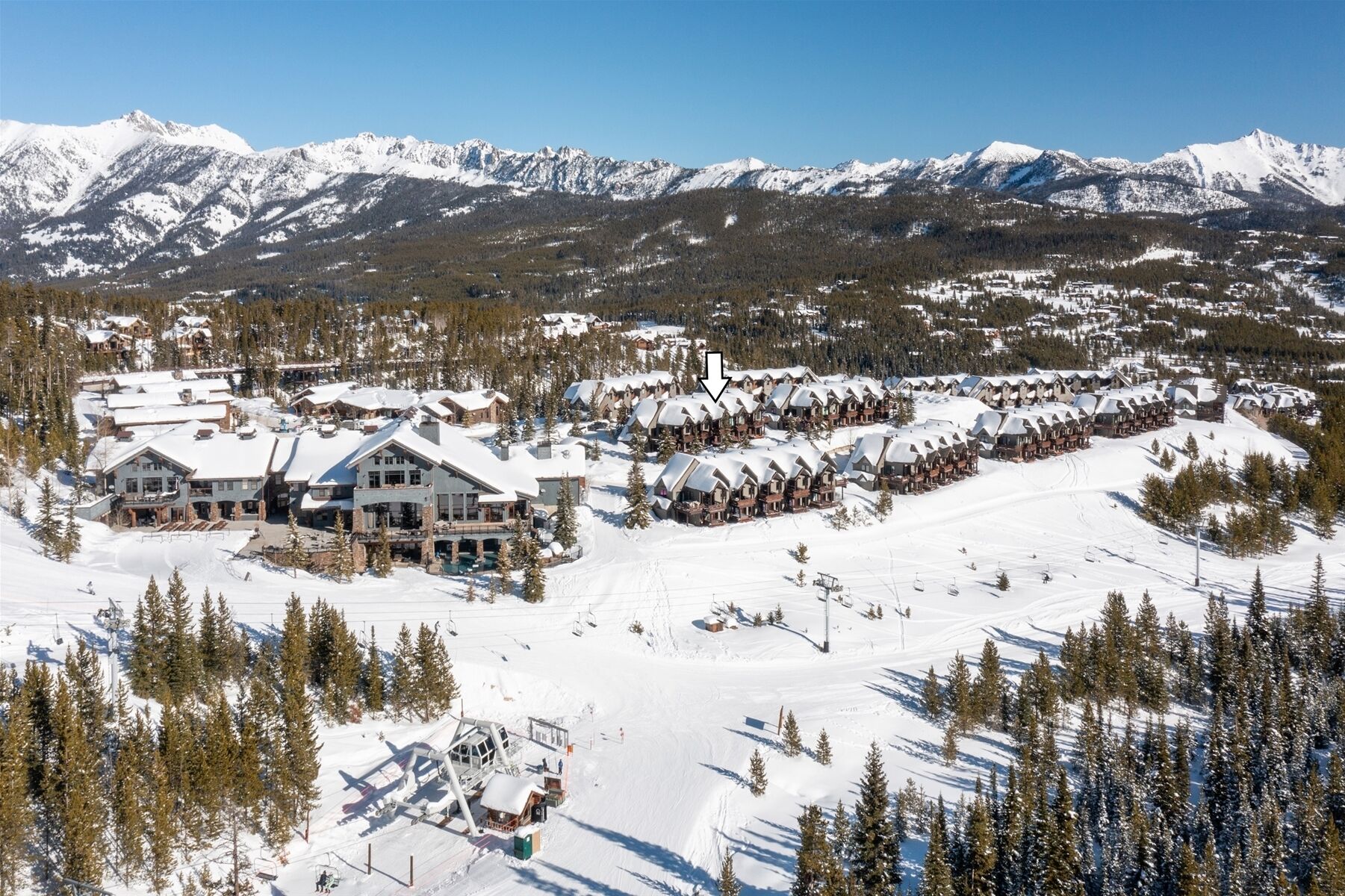 Une station de ski enneigée, avec plusieurs bâtiments de style chalet, des remontées mécaniques et un paysage montagneux en toile de fond.