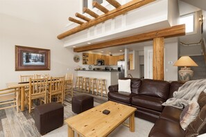 Un vaste espace de vie comprenant un coin repas avec une table en bois, un canapé en cuir et une cuisine à l’arrière-plan.