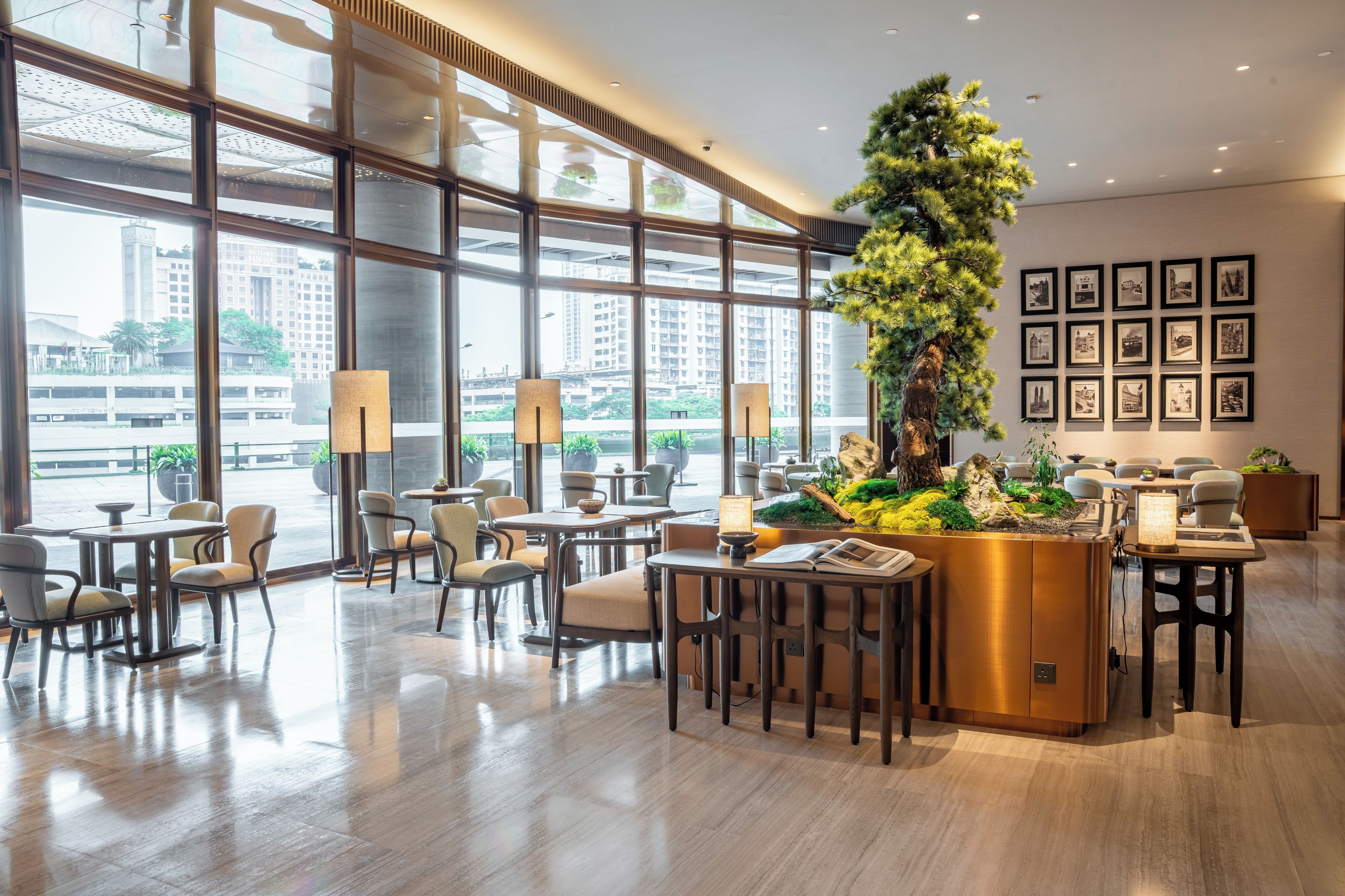 Un hall d’hôtel moderne, doté de grandes fenêtres, d’un grand arrangement floral au centre et d’un espace détente avec des tables et des chaises.