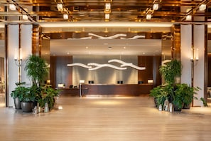 A modern reception area with a wooden reception desk, two potted plants, and a unique ceiling light fixture. - The Gardens Hotel - St. Giles Mid Valley Kuala Lumpur (Kuala Lumpur)