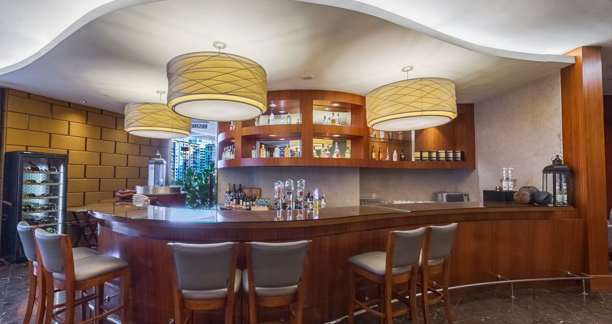 A bar area with a curved counter, multiple bar stools, and pendant lighting.