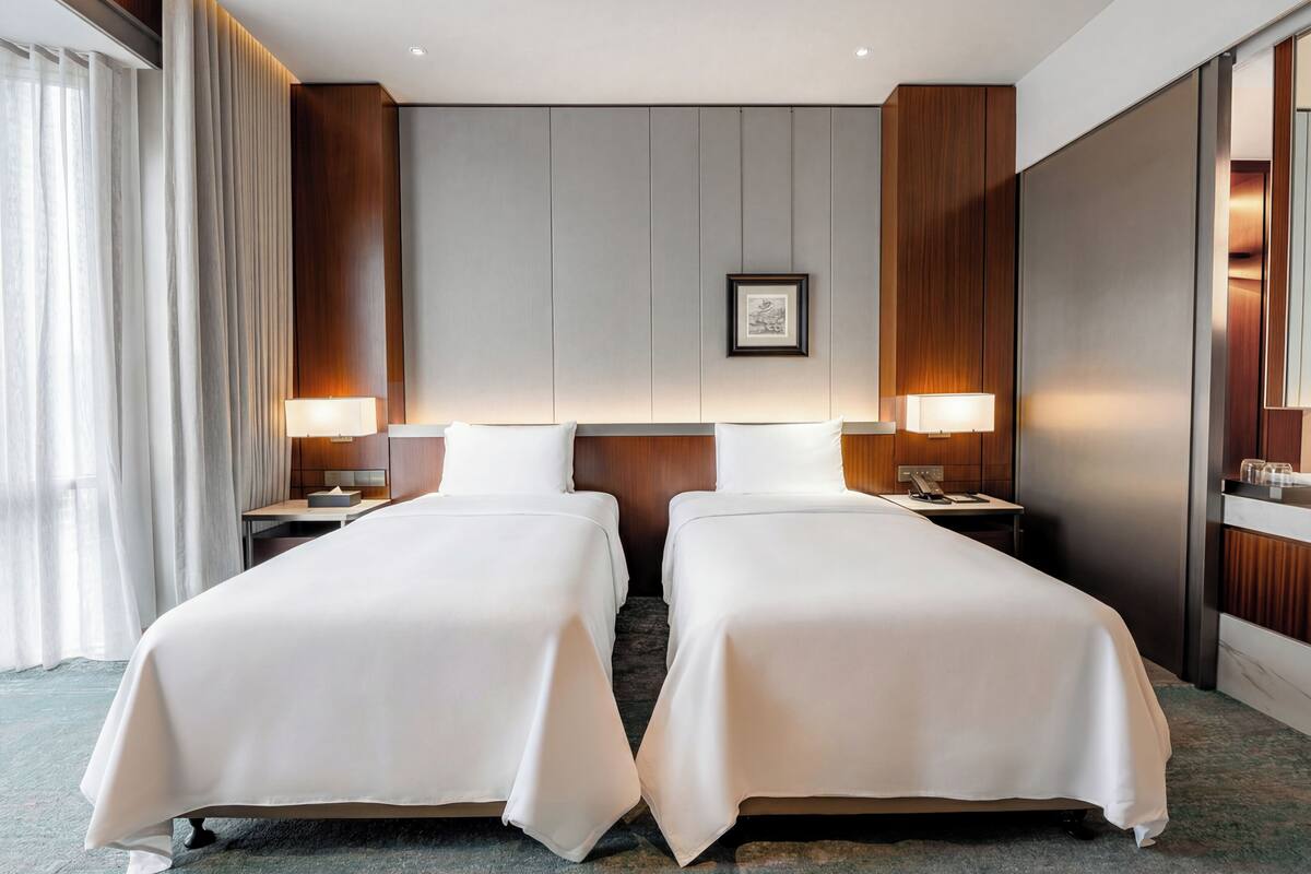 A hotel room with two beds, a framed picture on the wall, and a nightstand with a lamp.