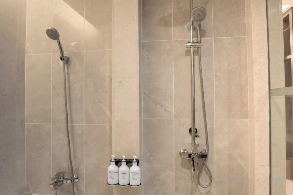 Un baño con dos cabezales de ducha, mampara de vidrio y tres botellas de champú.