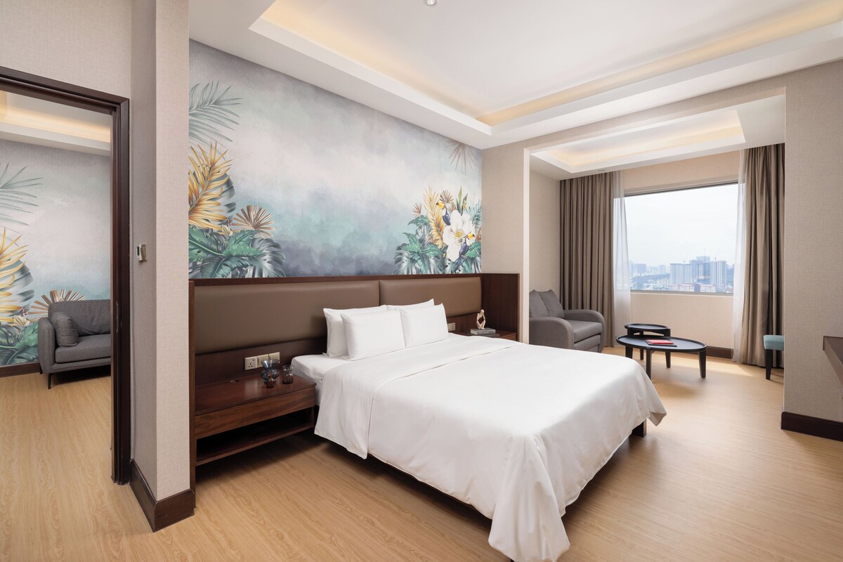 Una habitación de hotel con una cama grande, una mesita de noche, una zona de estar y vistas a la ciudad.