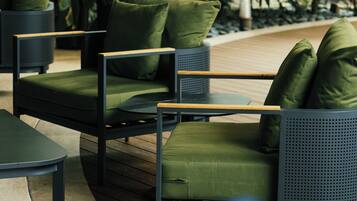 An outdoor seating area with a sofa and chairs, surrounded by potted plants.