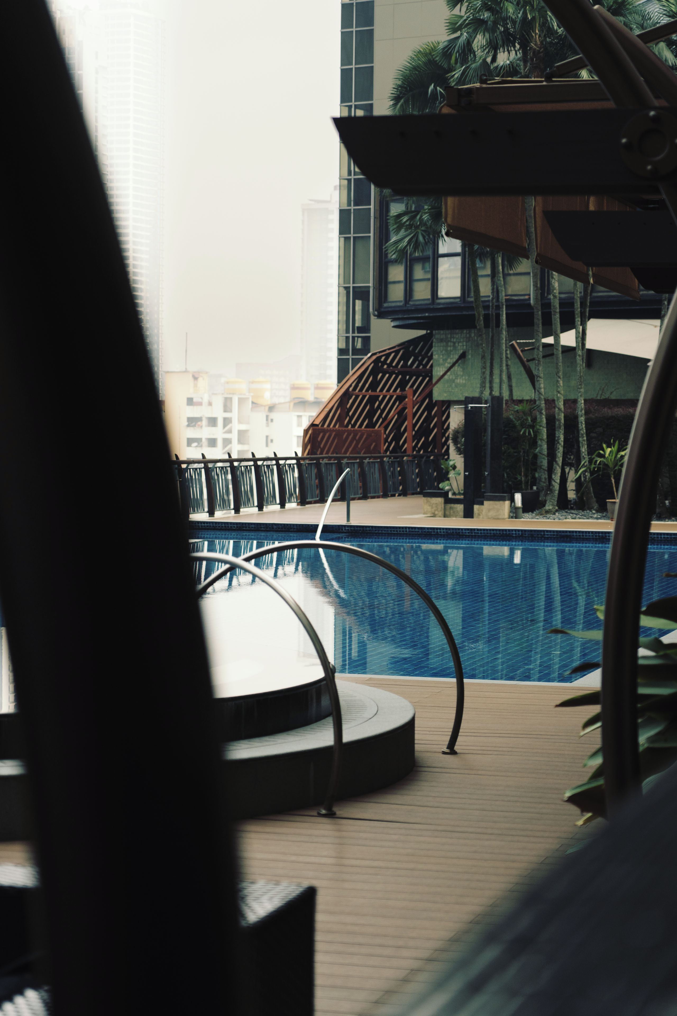 A pool area with a wooden deck, a metal pool edge, and a view of buildings in the background.