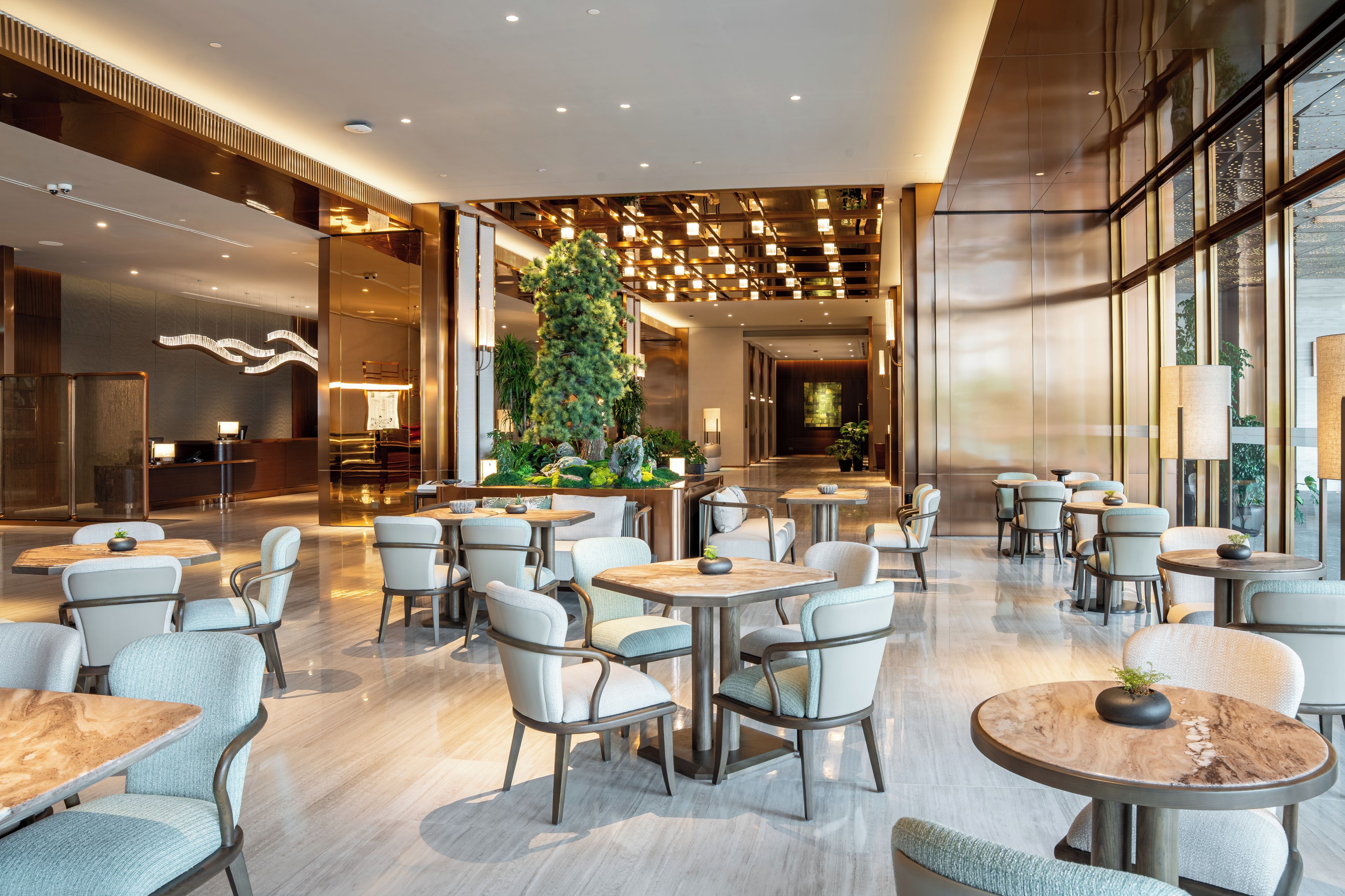 A modern interior with multiple seating areas, including round tables and chairs, and a central indoor plant arrangement.
