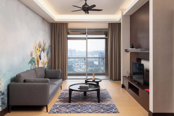 A modern living room with a sofa, coffee table, and TV stand, featuring a large window with a city view. - The Gardens Hotel - St. Giles Mid Valley Kuala Lumpur (Kuala Lumpur)