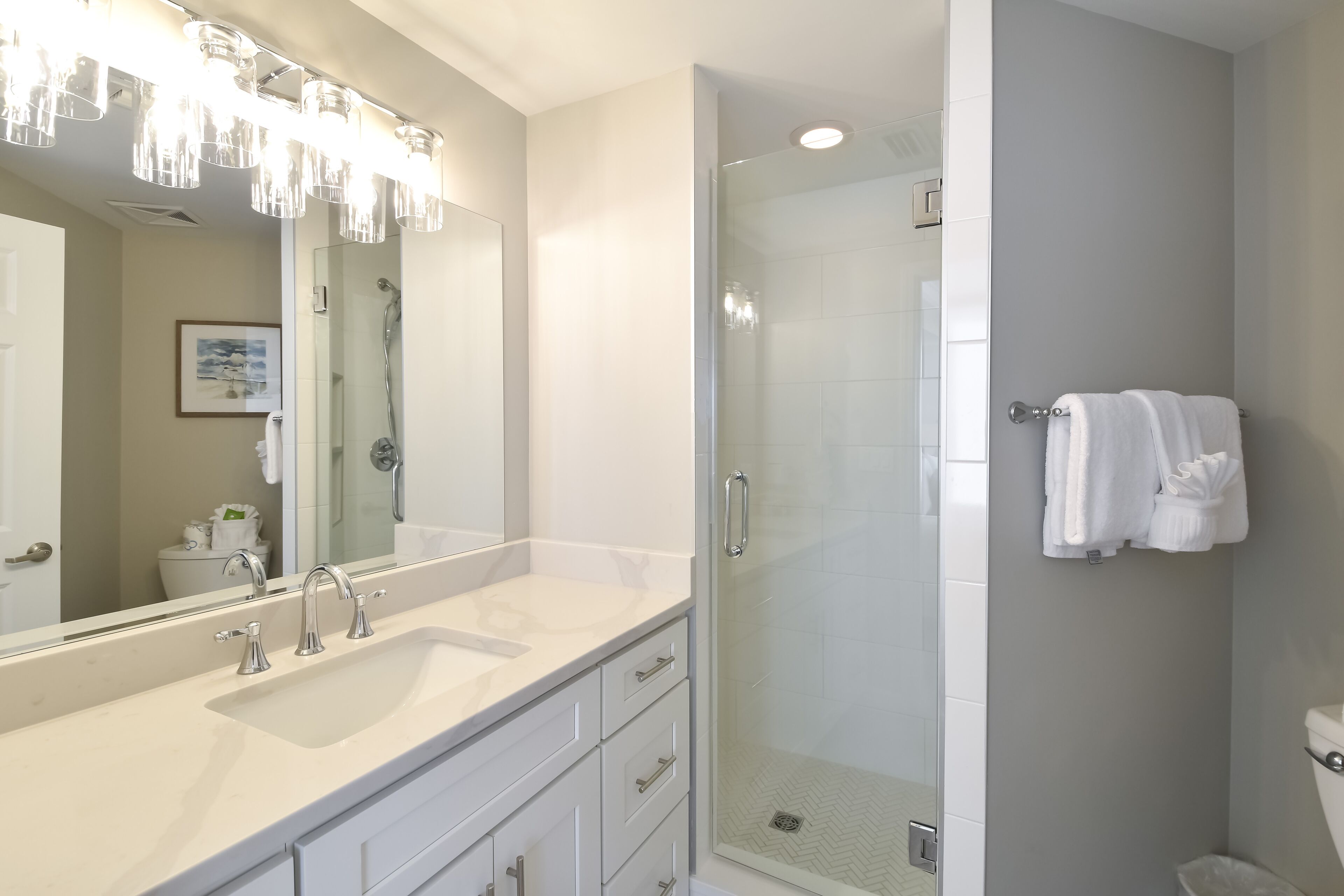A modern bathroom with a large mirror, two sinks, a glass-enclosed shower, and a towel rack.