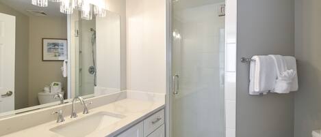 A modern bathroom with a large mirror, two sinks, a glass-enclosed shower, and a towel rack.