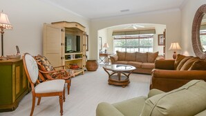 A spacious living room with a sofa, armchairs, a coffee table, and a television. - 3BR Golf Course Townhome | Community Pool, Full Kitchen & In-Unit Laundry (New Smyrna Beach)