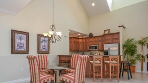 A spacious kitchen with wooden cabinets, a central island, and a dining area with striped chairs. - 3BR Golf Course Townhome | Community Pool, Full Kitchen & In-Unit Laundry (New Smyrna Beach)