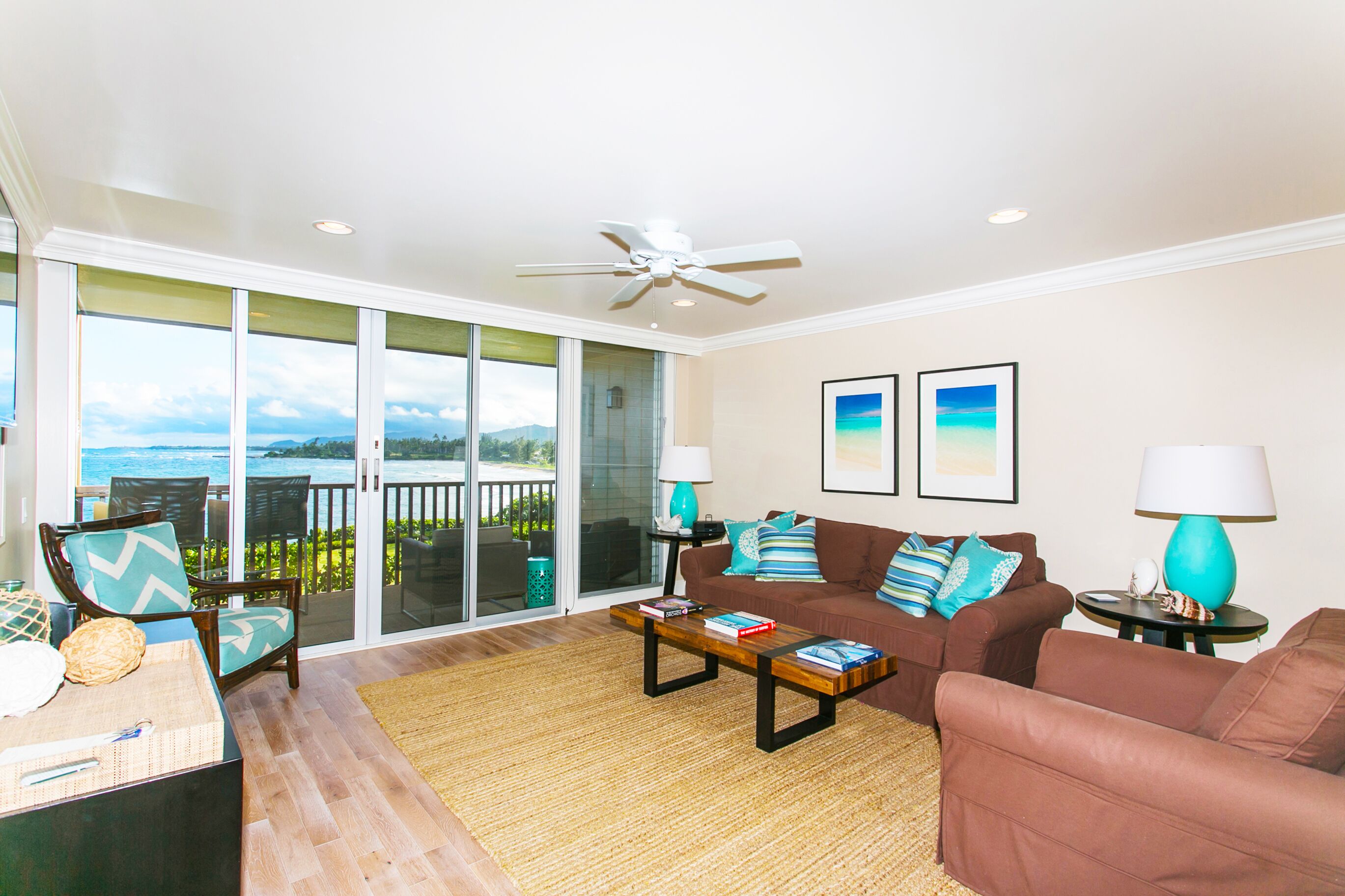 A spacious living room with a large sliding glass door leading to a balcony with a view of the ocean. There are two couches, a coffee table, and two lamps.