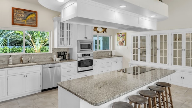 Una cocina moderna con armarios blancos, encimera de granito y una isla grande con taburetes de bar.