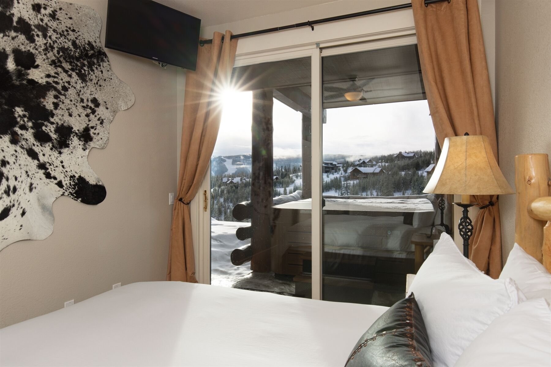 Ein Hotelzimmer mit Bett, großem Fenster mit Vorhängen, einem an der Wand befestigten Fernseher und einem Kunstwerk aus Rindsleder.